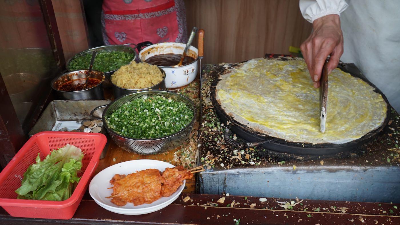 My favorite street food of all time. I barely know what the name means in Chinese so I have no clue what it would translate to in English. Some kind of crepe-like thing, seasoned with a bunch of stuff, with a crunchy thing in the middle.